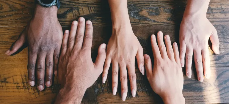 Six diverse hands placed side by side on a wooden surface